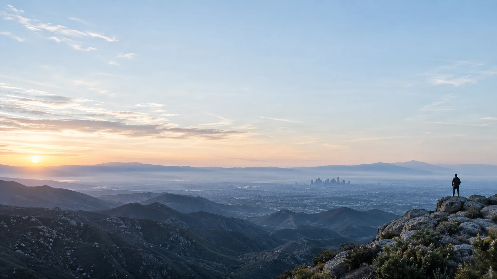 A person looks across a sunlit mountain landscape toward a distant city.